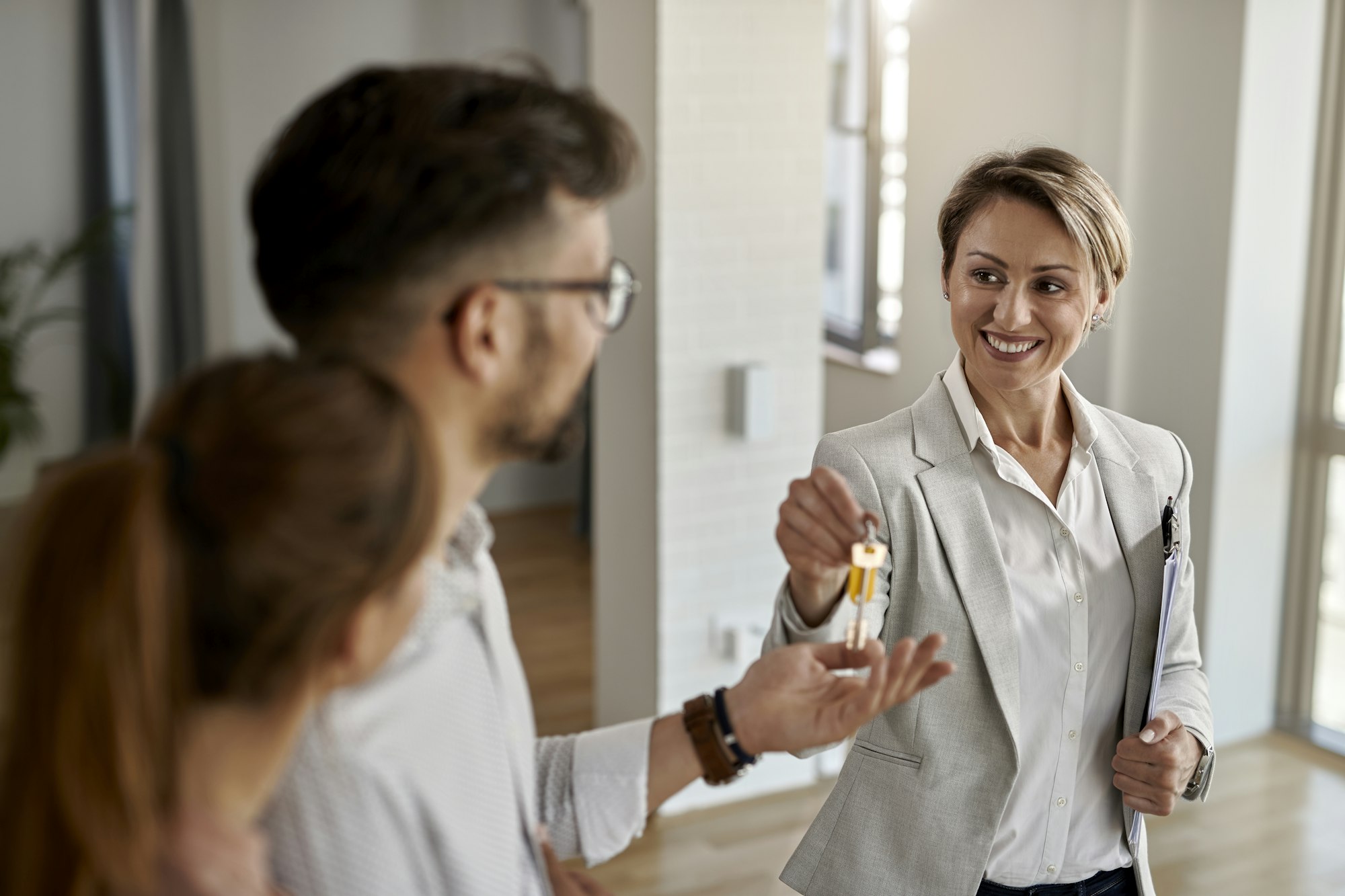 Happy real estate agent giving to couple keys of their new home.